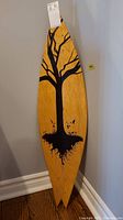Top view of longboard showing tree and roots painted in black on natural wood finish.