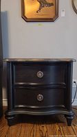 Front view of one black wood veneer nightstand showing 2 drawers with brushed chrome pulls and curved legs.
