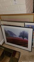 Five stacked framed art prints leaning against a wall, visible sizes from small to medium frames.