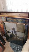 Photo of 4 large framed posters stacked leaning against a wall, varying sizes and frames visible.