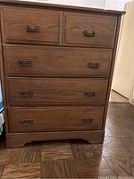 Front view of wooden chest of drawers showing five drawers with metal handles