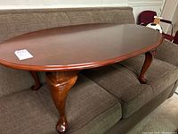 Photo showing the oval wooden coffee table with smooth brown surface and cabriole legs from one angle, placed on a sofa.