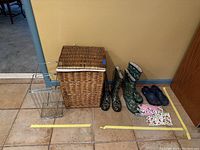 Wicker basket hamper, two metal shelf risers, two pairs of camouflage yard boots, three pairs of colorful garden gloves, and one pair of dark blue Crocs.