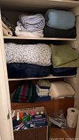 Shelves with multiple folded blankets, towels, and a box containing cleaning supplies and paper towels.