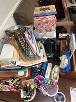 Wide view of office supplies lot showing file organizers, colored pens and pencils, decorative photo boxes, hangers, staplers, and other stationery items on a desk.