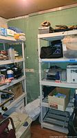 Two white plastic storage shelves filled with assorted household items in a basement corner, showing their height and condition.