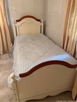 Twin wooden bed frame with white paint and natural wood top accents, dressed with patterned comforter and linens, placed between curtains.