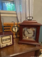 Photo showing all three items: Numechron flip clock, Crosley wooden radio with antenna, and Bulova mantel clock with brass Roman numerals and decorative wood finish.