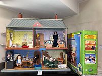 Front view of vintage Madeline dollhouse with original box visible to right side. Dollhouse contains furnishings and dolls including a nun figure and children in Madeline costumes.