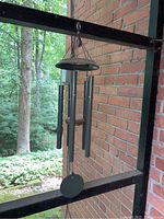Clear view of the two hanging metal tube wind chimes against a brick wall and greenery background.