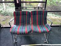 Front view of the wrought iron glider with green, red, blue and white striped cushions in outdoor screened porch.