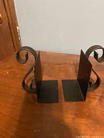 Pair of metal bookends with curved decorative ends positioned upright on a wooden table.