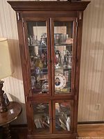 Full view of the closed wooden display cabinet, showing dual glass doors on upper and lower sections, wood frame with crown molding and base.