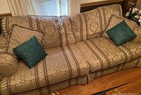 Beige patterned fabric couch with decorative teal pillows, photographed to show upholstery and condition.