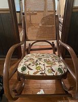 Front view showing the cane backrest and floral fabric seat cushion on wooden curved frame.
