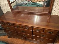 Photo of a dark wooden dresser with nine drawers and attached large rectangular mirror on top. The dresser shows general surface wear.