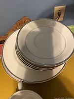 Stacked small plates and saucers with a visible teacup handle at bottom, showing white china with silver trim rim.