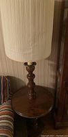 Image showing the tall table lamp with wooden turned base and cream pleated lampshade on a polished round wooden side table.