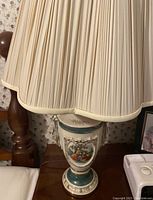 Close-up view of ceramic lamp base with painted detailed nature scene and beige pleated fabric lampshade.