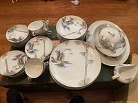 Full set of dinnerware laid out on table showing plates, cups, sugar dish, creamer, serving bowls and dish.