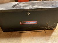Full view of the black steel trailer tongue box with lock and label visible.