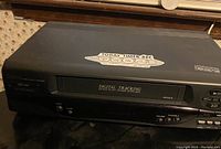 Black Samsung VCR VHS player with digital tracking and timer record features visible on front panel and a label on top.
