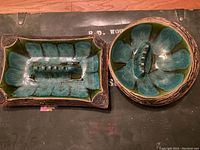 Photo showing two ceramic ashtrays, one rectangular and one round, both with blue-green glaze and textured leaf pattern, rectangular one chipped