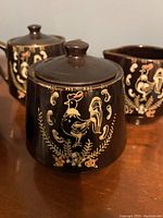 Close-up photo of sugar bowl showing hand-painted rooster and floral design on dark brown ceramic