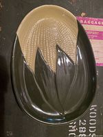 Top-down photo of a vintage ceramic platter shaped like an ear of corn with green husks and yellow kernels.