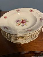 Stack of white porcelain soup bowls showing embossed rim, floral pattern and gold gilt trim