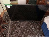 Front view of the 50 inch flat screen TV standing on its legs on a patterned carpet floor showing its slim profile and black frame.