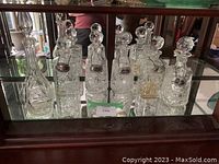 Six crystal decanters and serving bottles displayed with solid silver tags on four decanters and one serving bottle. Pinwheel pattern cut into crystal. Glass stoppers present on all items.