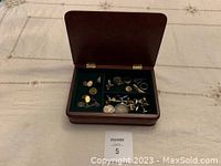 Overview of the small wooden jewelry box open, showing assorted jewelry items inside including rings, cufflinks, and chains.