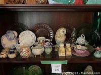 Photo of one wooden shelf showing assorted vintage porcelain items including salt and pepper shakers, tea service pieces, a porcelain owl figurine, a broom doll, and several glass plates behind them.