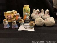 Front view of the 12 assorted vintage salt and pepper shakers displayed on a black cloth background showing variety in design including floral, character, and novelty shapes.