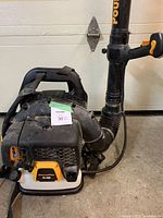 Black and orange gas-powered Poulan Pro backpack leaf blower model PBX 65SI with visible straps, throttle handle, and flexible blower tube, photographed on concrete floor near a garage door.