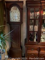Full front view of grandfather clock next to china cabinet