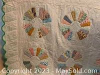 Close-up of hand-stitched quilt showing detailed circular patchwork design on white background with scalloped green edging