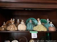 Wooden shelf top row showing seven half-doll pincushions in front of four decorative glass plates.