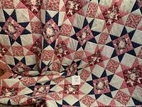 Quilt laid out showing detailed patchwork star and floral pattern in red, white, and blue tones.
