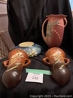 Photo of four Roseville pottery pieces against black background: one tall vase, one blue bowl, two matching wall hangings.