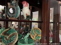 Wooden shelf holding five ceramic pieces: fish pitcher and rooster pitcher on top; two leaf bowls and a parrot bowl on bottom