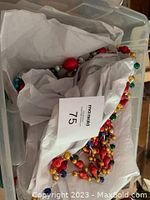 Plastic bin with tissue paper containing coiled strands of colorful vintage glass garland beads in red, teal, gold, and blue.