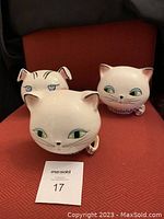 Three white ceramic cat head string holders on red upholstery