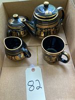 Full set of four black ceramic pieces with gold Greek design inside a cardboard box.