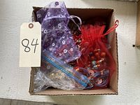 Overhead photo of box with multiple organza bags and plastic bags containing red, purple, and natural stone colored necklaces and bracelets.