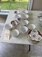 Top-down photo showing 10 porcelain tea cups arranged with matching saucers stacked separately, all on a white table.