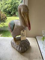 Front view of the hand-painted clay pelican statue with visible painted detail and standing on rock base.