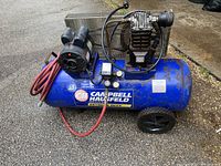 Front view of blue Campbell Hausfeld air compressor with tank, motor, and red air hose coiled on the side. Shows unit is portable with wheels.