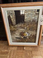 Framed oil painting showing barn door with flowers on the ground and in a bouquet, under natural light, photographed from front.